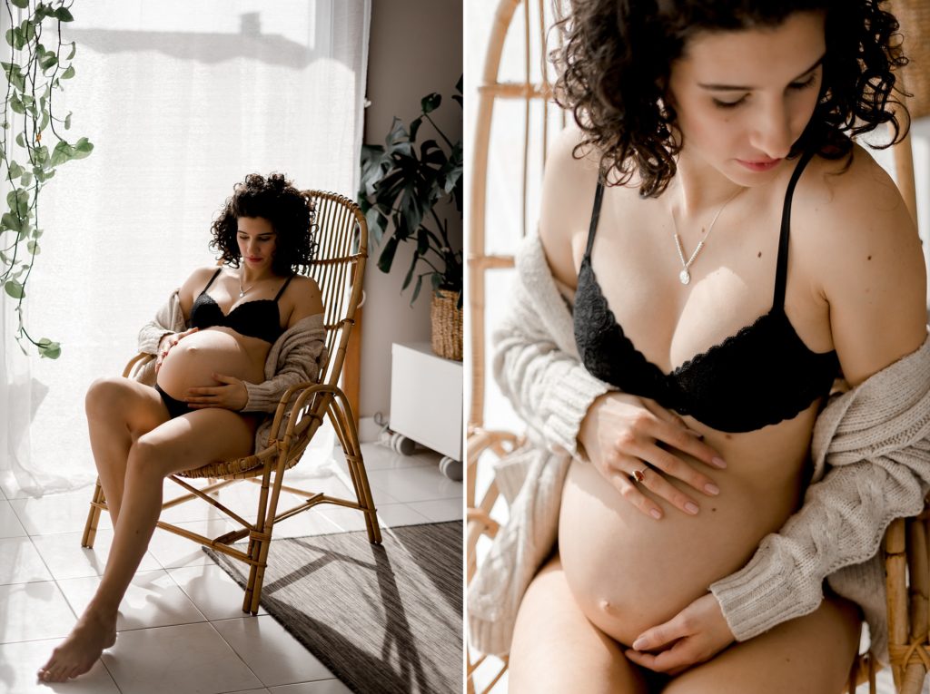 Femme enceinte assise dans un fauteuil en rotin et portant un gilet beige ouverte sur de la lingerie noire lors d'une séance photo maternité à Niort