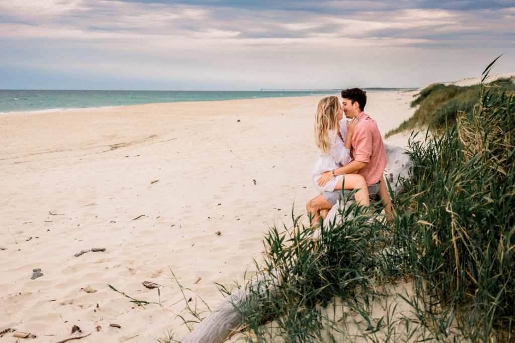 Un couple s'embrasse sur un tronc d'arbre sur une plage lors de leur séance photo dans les Landes