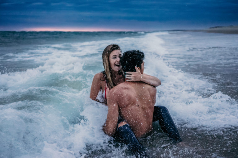 Couple se faisant éclabousser par des vagues lors de leur séance photo.