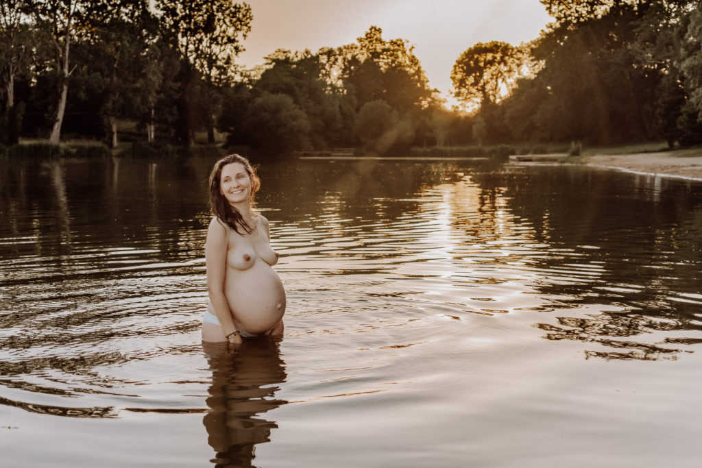 Femme enceinte nue dans un lac au coucher du soleil