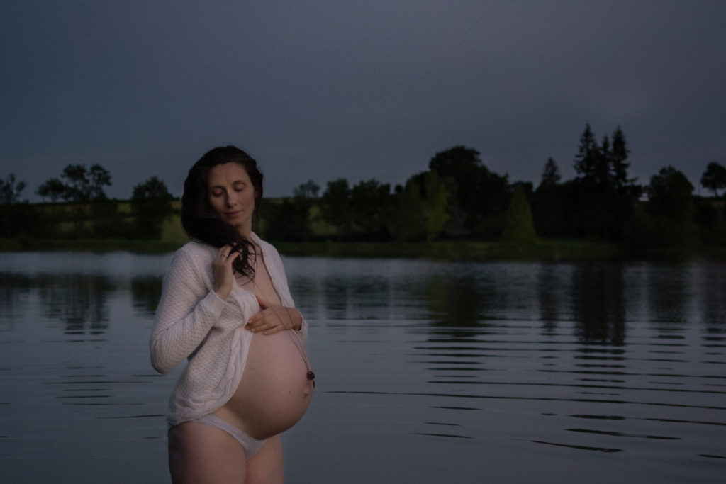 Femme enceinte portant un gilet ouvert sur son ventre lors d'une séance photos de maternité dans un lac