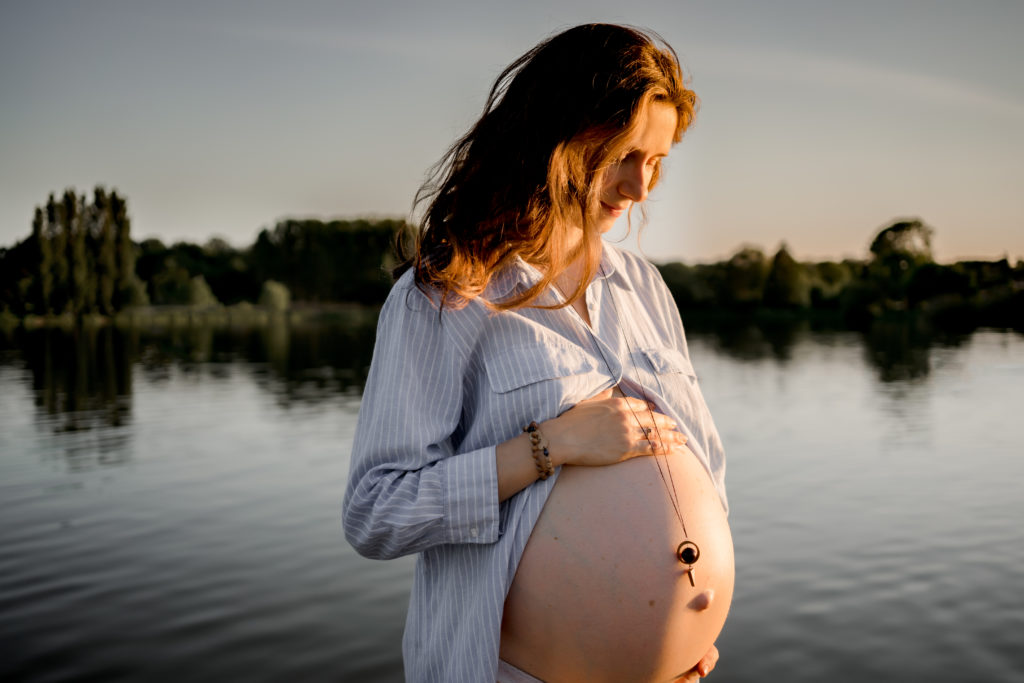 Femme enceinte portant une robe longue ouverte sur son ventre lors d'une séance photos de maternité dans un lac