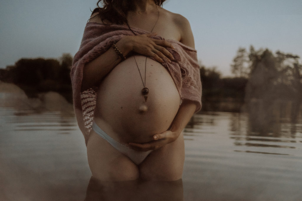 Femme enceinte portant un châle tricoté vieux rose sur ses épaules lors d'une séance photos de maternité dans un lac avec de la brume