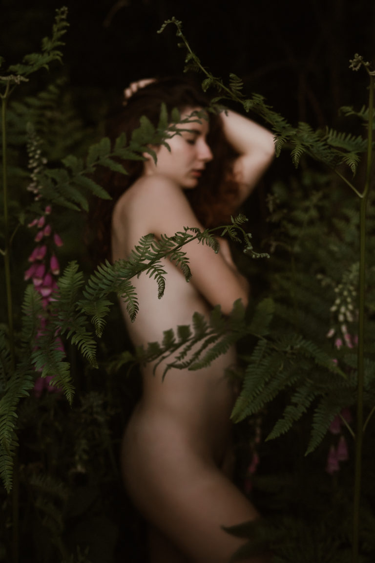 Photo d'une femme en train de poser nue debout de profil parmi des fleurs et des fougères